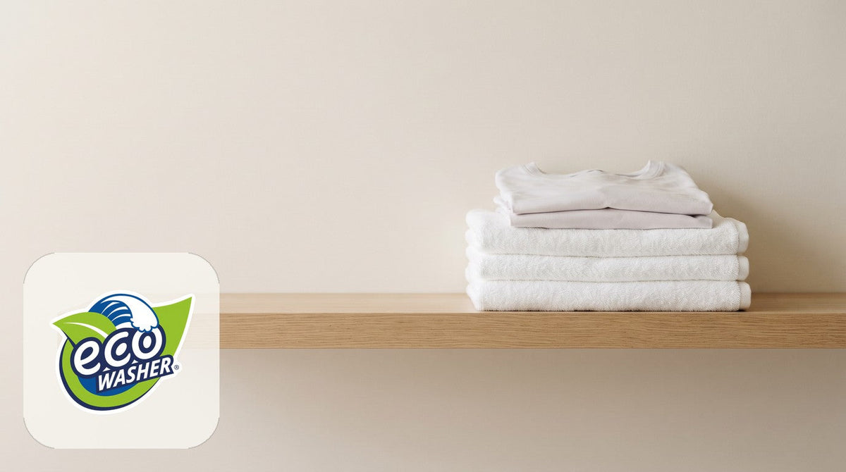 White towels and folded white tees stacked on a light oak shelf against a cream wall