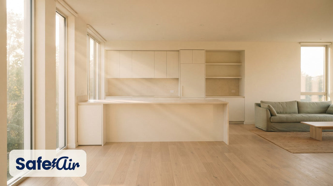 Sunlit open cream kitchen with a bare island and a sage sofa in the living area.
