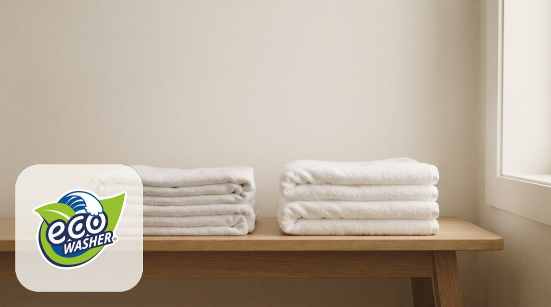 Two stacks of folded white towels on a light oak bench in front of a cream wall.