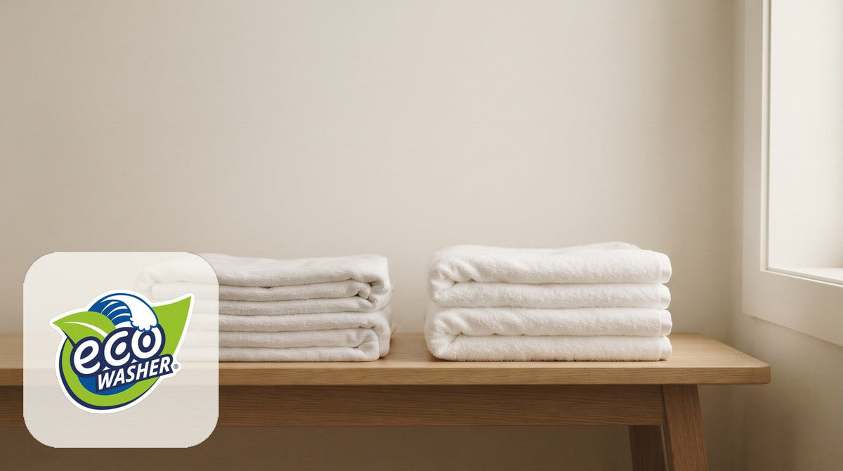 Two stacks of folded white towels on a light oak bench in front of a cream wall.